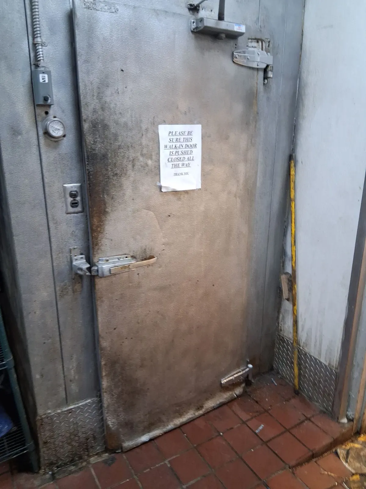 Worn walk-in freezer door that will not latch, with a sign asking staff to push it closed