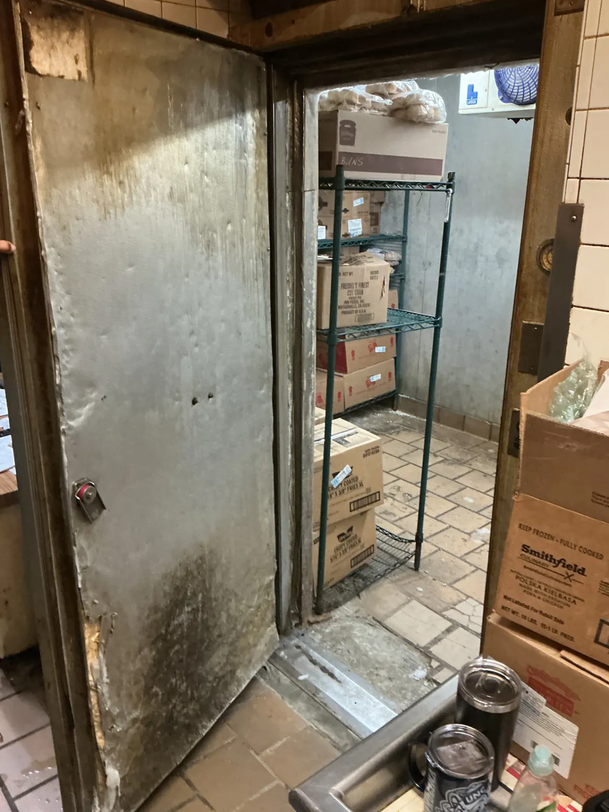 Damaged walk-in freezer door with a delaminated lower panel and bent frame